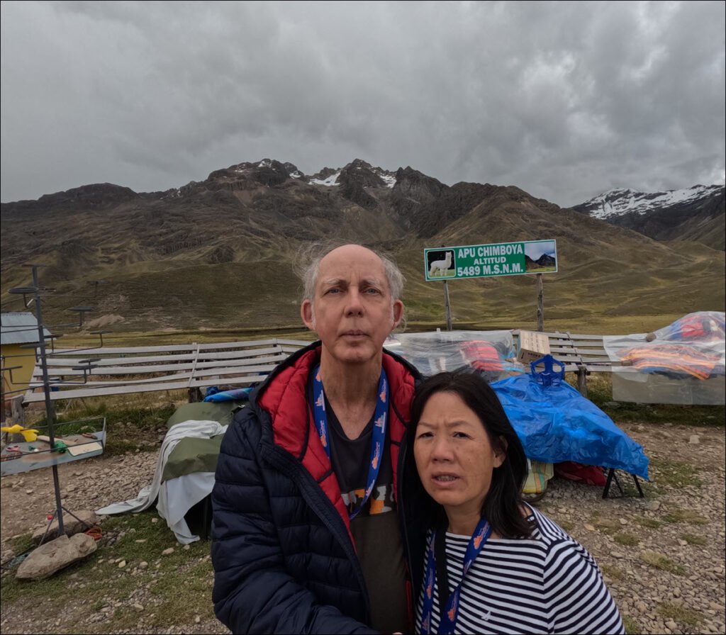 Ron and Winnie looking at the camera, with a road sign "Apu Chimboya" elevation 5489 MSNM, equals 18,008 feet above sea level.
