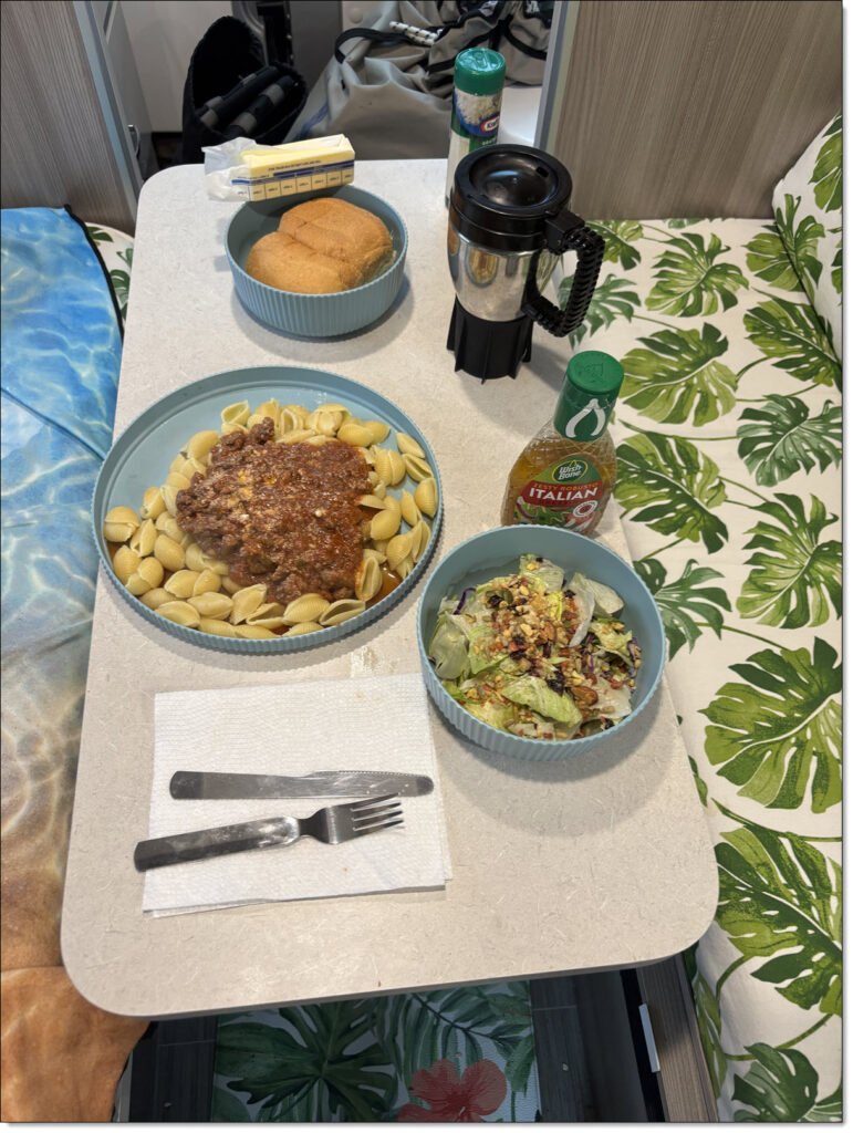Basic RV camping dinner of pasta shells with meat sauce, rolls, and salad.