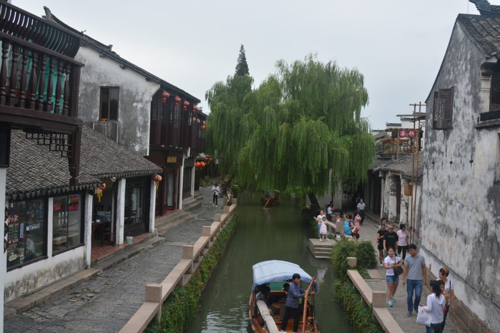 a narrow canal with shops on the left side and a stone wall on the right side with a pedestrian walkway. 