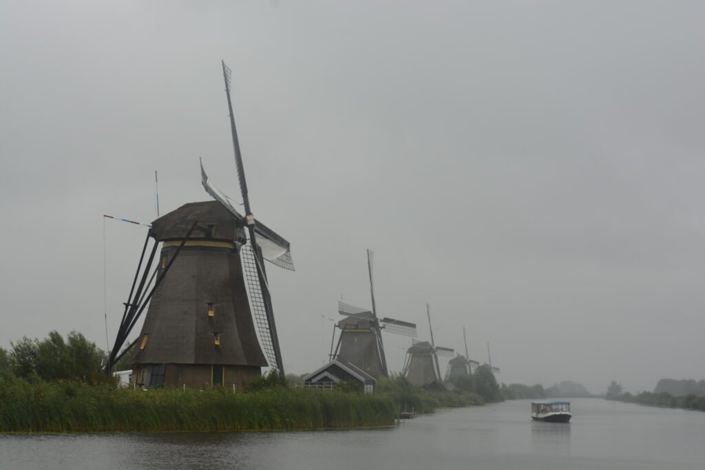 a wide canal with dutch windmills on the left and a small canal boat in middle of the canal