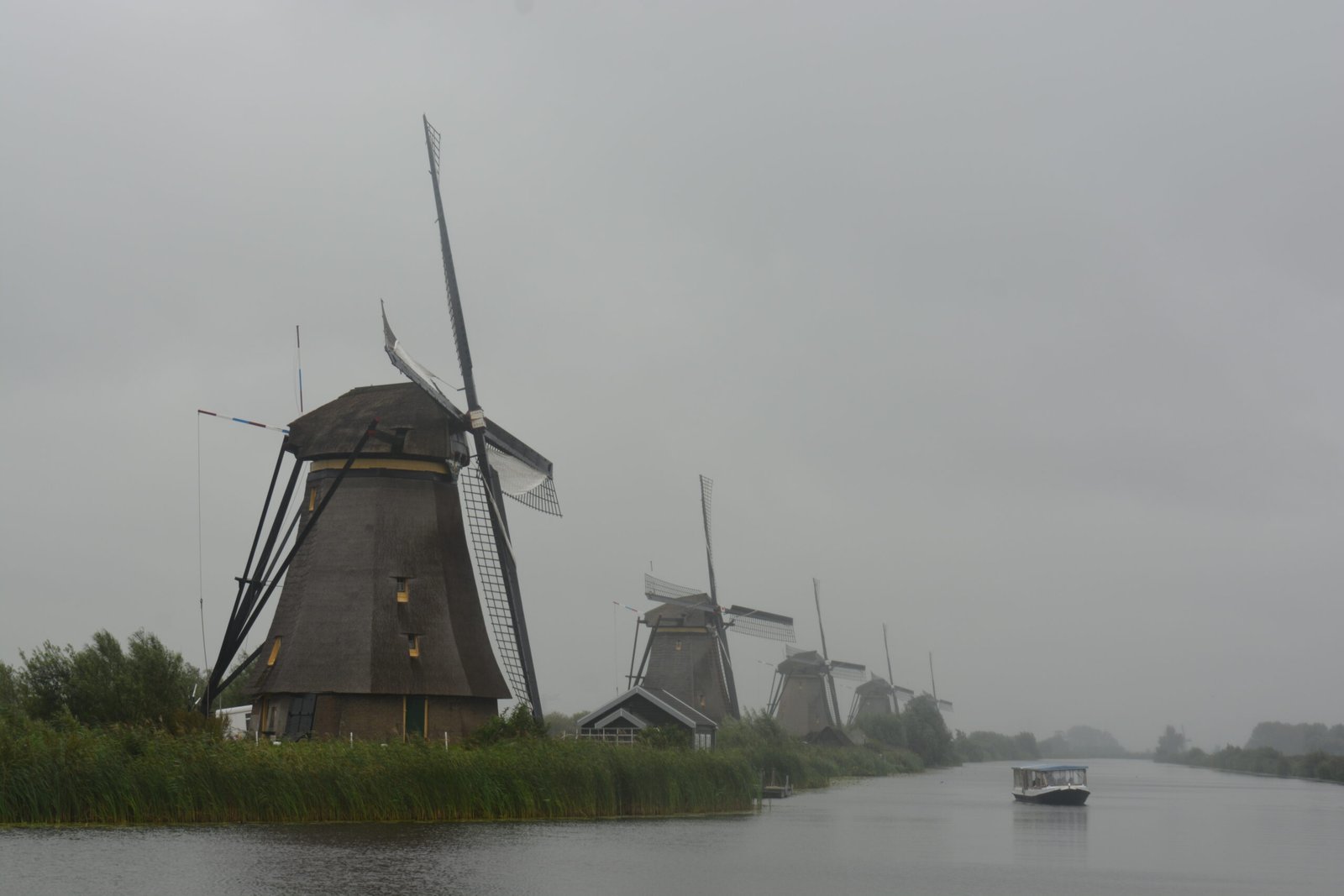 a wide canal with dutch windmills on the left and a small canal boat in middle of the canal