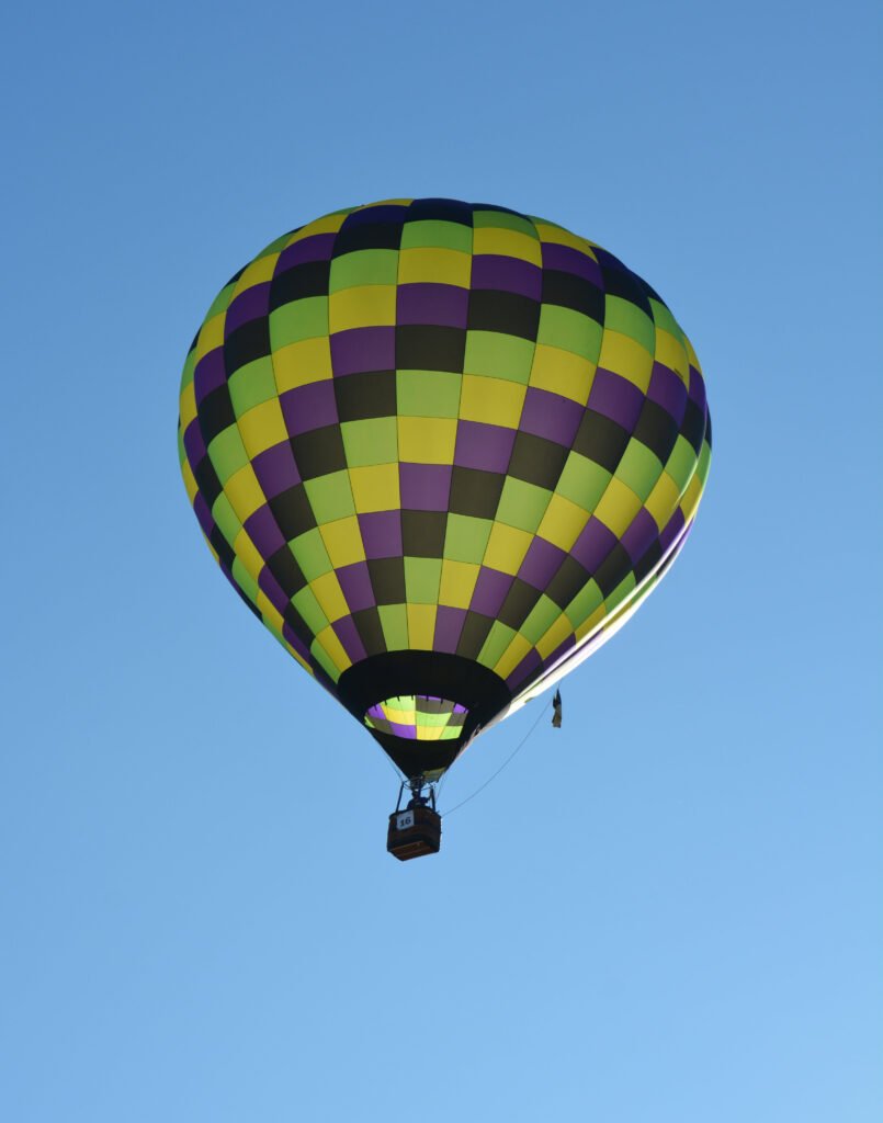 A tile-patterned multicolor hot air balloon suspended in a clear blue sky, glowing from sunlight behind it. Ron Charest's entry into the 2026 senior games digital photography event.  