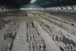 Rows of Terracotta Warriors Rows of trenches showing rows of grey figures of ancient chinese warriors inside a large domed building.