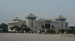 A large building in stylized modern chinese design of white stone. A large plaza in front