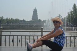 Winnie Taking A Break woman sitting in front of a large plaza water display with a pagoda in the background.