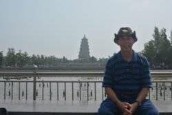 Ron Taking A Break man sitting in front of a large plaza water display with a pagoda in the background.