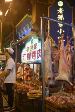 Nightlife in the Muslim Quarter of Oldtown Xi'an a young man stands in front of a butcher's market stand with a pig carcass hanging from a rack.