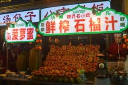 Nightlife in the Muslim Quarter of Oldtown Xi'an a night time stand with different types of cut fruit and a full jack fruit, with older man standing behind the stand.
