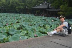Ron and The Field of Lotus A man wearing a brimmed hat sitting on a wall next to a field of lotus plants