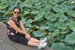 Winnie and The Lotus Plants Woman wearing sunglasses sitting on a wall next to a field of lotus plants