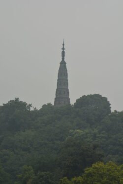 The Baochu Pagoda in Hangzhou a tall, narrow-diameter conical tower with antenna structure at it's point, mounted on top of a hill. Looking through haze