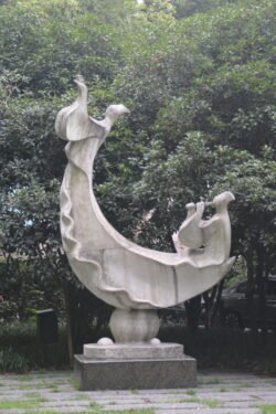 A Sculpture Along West Lake in Hangzhou a stone sculpture of a stylized boat with two riders in front of a glade of smjall trees.