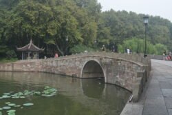 a stone arch bridge with a pedestrian walkway over it, a small Chinese-roofed pavilion at the far end.