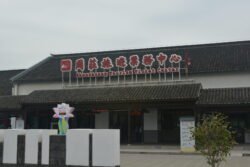Tourist Entrance to The Water Town of Zhouzhuang modern building with chinese lettering and underneath the sign "Zhouzhuang Tourist Ticket Center" in english