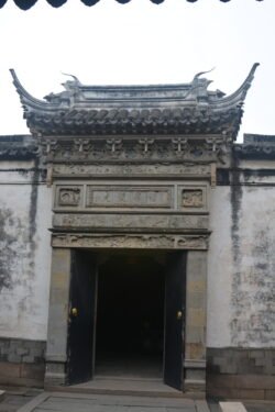 a wide doorway set into a dirty-white stone wall topped with traditional chinese roof