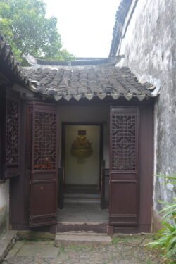 a small door flanked by ornate carved brown panels leading into a small room with a wall sculpture, covered with a tile roof