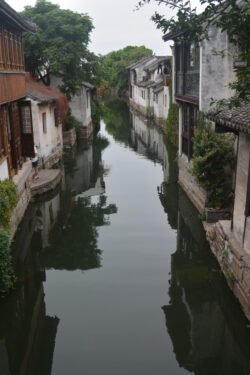 narrow canal lined by stone houses on either side. The buildings are reflected in the still water of teh canal