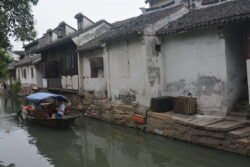narrow canal with canal boat and the back side of houses on left side.