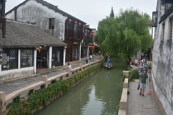 a narrow canal with shops on the left side and a stone wall on the right side with a pedestrian walkway.