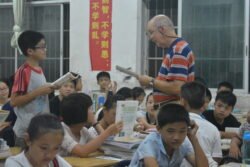american man standing in front of a teenaged Chinese boy, both are holding books