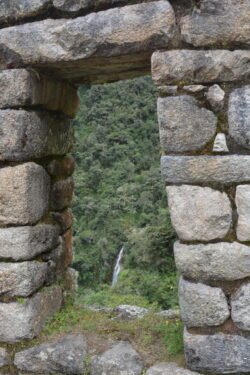 An Inca-style stone doorway looking out on a spring-fed waterfall.