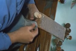 A pair of hands creating a small oval piece of carved shell