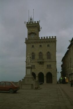 A tall medieval building topped with a tower on one corner standing alone at top of a hill.