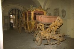 An ornate, gilded wood carriage displayed in a museum.
