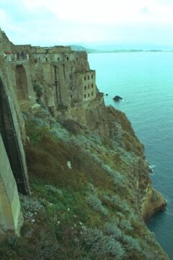An ornate palace on the side of a steep cliff with the ocean below.