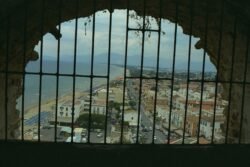 A View of a seaside town with white beaches and a small town, through a metal grill from a height above the ground.