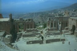 Ruins of a theatre with stage in front of stone columns, and a mountain in the background.