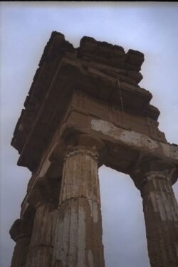 Three columns forming a corner of an ancient building with ornate stone capstones connecting the three columns