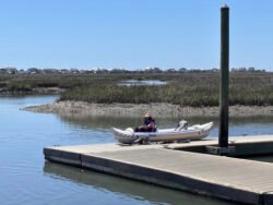 Sea eagle 370 inflatable kayak, sitting on a pier with woman sitting inside, salt marshes in background.