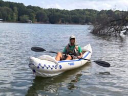 Man in a fishing hat wearing sunglasses Kayaking on Lake Norman, holding a paddle