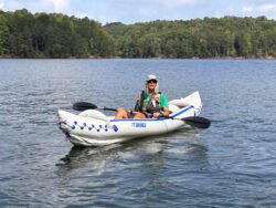 Man wearing a fishing hat and sunglasses in a white inflatable kayak, holding a paddle.