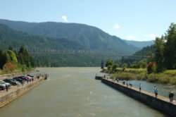 a wide river lock with steel bridge crossing a wide muddy river, mountains in the background.