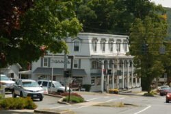 a white two story building with porch columns on lower level and large windows on upper level, in a roadway intersection