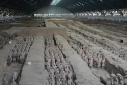 excavated trenches inside a large building with formations of terracotta warriors standing in the trenches