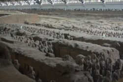 excavated trenches inside a large building with formations of terracotta warriors standing in the trenches