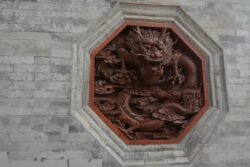 A Red Dragon of Daci'en Temple complex in Xi'an, China. A octagon framing a chinese-style red dragon carved into a light grey stone wall.