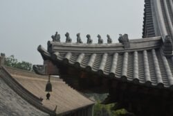 Details of a Temple Roof detailed view of a traditional chinese temple roof. The ridge of the roof is decorated with a series of small, molded figures. A small bell hangs from the wooden beam of the eave