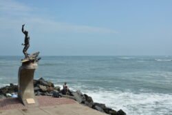 A bronze statue of a man surfing on a wave, mounted on Makaha Beach of Lima Peru
