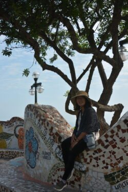 Winnie Charest sitting on a colorful wall with a tree and blue sky behind her.