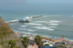 Looking down from the top of coastal cliffs to a lovely pacific beach with restaurant on a long pier. Miraflores District, Lima, Peru