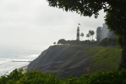 A black and white striped lighthouse perched on the edge of steep coastal cliffs overlooking the ocean