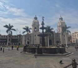 Large bronze fountain in a large open city plaza. A large catholic cathedral is in the background.