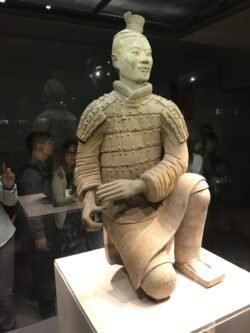 a kneeling terracotta Warrior inside a protective glass case