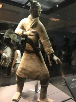a detailed terracotta figure in a martial arts fighting pose in a protective glass case