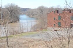 a view of the Erie Canal with a field in the foreground and large red brick building on the right side.