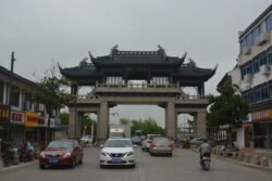 a ornate chinese-style archway across a modern roadway with cars and bicycles entering and leaving through the gate